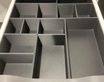Könnte beinhalten: Ein grauer Schubladenorganizer mit mehreren Fächern in verschiedenen Größen. Der Organizer ist aus einem strukturierten Kunststoffmaterial.