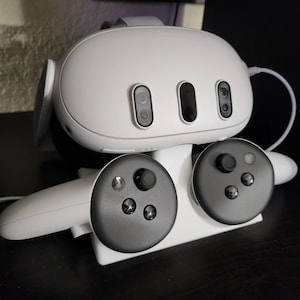 Op de afbeelding: Een witte VR-headset met twee zwarte controllers. De headset heeft twee camera's aan de voorkant en een witte band. De controllers hebben een zwarte knop in het midden en vier andere knoppen eromheen.