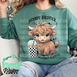 May include: A green sweatshirt with a cartoon illustration of a brown and white cow with the text "Moody Heifer Without Coffee".