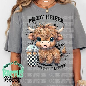 May include: Gray t-shirt with a cartoon illustration of a brown and white Highland cow with the text "Moody Heifer Without Coffee" printed on the front.