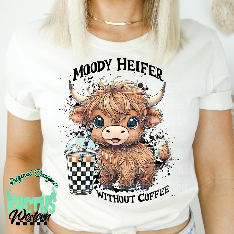 May include: White t-shirt with a cartoon illustration of a brown Highland cow with a black and white checkered cup of iced coffee. The text "MOODY HEIFER WITHOUT COFFEE" is printed on the shirt.