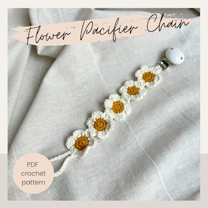 May include: A white crocheted flower pacifier chain with yellow centers. The chain is attached to a white plastic clip. The text "Flower Pacifier Chain" is written in black on a pink background. The text "PDF crochet pattern" is written in black on a white circle.