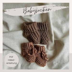 Könnte beinhalten: Zwei Paar braune gestrickte Babyschuhe und -socken werden auf einem neutralfarbenen Stoff gezeigt. Das obere Paar ist dunkler braun, während das untere Paar einen helleren Farbton hat. Der Text "Babysocken" und "PDF Häkelanleitung" sind sichtbar.