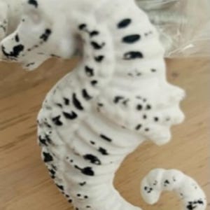 May include: White ceramic seahorse figurine with black painted details. The seahorse is curled in a classic pose with a textured surface.