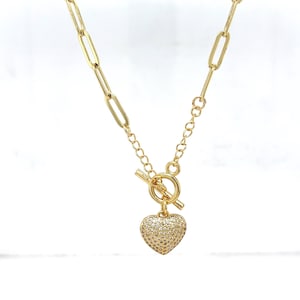 Op de afbeelding: Goudkleurige ketting met een hartvormige hanger. De hanger is bezet met kleine, sprankelende steentjes. De ketting heeft een tuimelsluiting en een ketting met langwerpige schakels.