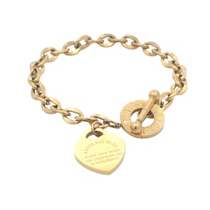May include: Gold-toned bracelet with a chain link design. A heart-shaped charm dangles from the chain, engraved with the words "ABOVE ALL ELSE. GUARD YOUR HEART, FOR EVERYTHING YOU DO FLOWS FROM IT." The bracelet has a toggle clasp with the inscription "4:23 FOREVER".