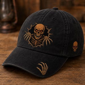 May include: A black baseball cap featuring an embroidered design of a skeleton emerging from a jagged hole on the front panel. The skeleton has glowing orange eyes. A small skeleton hand is embroidered on the brim and a skull on the side.