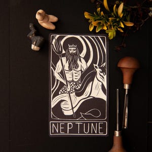 May include: Black and white linocut print depicting Neptune, the Roman sea god, with a trident. The word "NEPTUNE" is printed below. The print shows a detailed illustration of Neptune wearing a crown and a long beard.