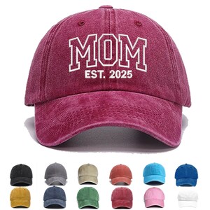 Könnte beinhalten: Burgunderfarbene Baseballkappe mit dem Wort "MOM" in weißen Buchstaben und dem Text "EST. 2025". Die Kappe hat einen gebogenen Schirm und einen Used-Look. Zusätzliche Kappenfarben werden darunter angezeigt.