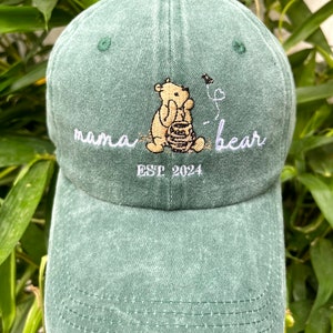 May include: Green baseball cap with an embroidered image of Winnie the Pooh holding a honey pot. The text "mama bear" and "EST 2024" is also embroidered on the cap.
