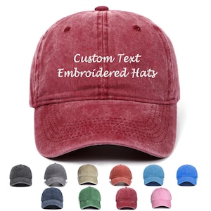 Könnte beinhalten: Eine kastanienbraune Baseballkappe mit verwaschenem Finish und dem weiß gestickten Text Custom Text Embroidered Hats auf der Vorderseite. Unter der Hauptkappe sind zwölf weitere Baseballkappen in verschiedenen Farben abgebildet.