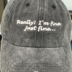 K&ouml;nnte beinhalten: Eine schwarze Baseballkappe mit dem Text "Really! I'm fine, just fine..." in wei&szlig; gestickt.