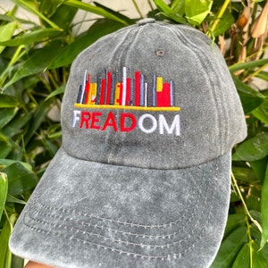 May include: A gray, distressed, baseball cap with an embroidered cityscape design and the word "FREEDOM" in red and white lettering.