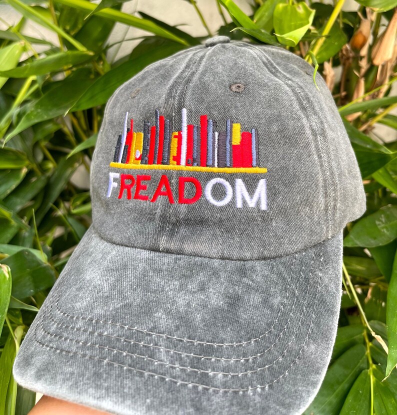 May include: A gray, distressed, baseball cap with an embroidered cityscape design and the word "FREEDOM" in red and white lettering.