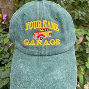 Könnte beinhalten: Eine grüne Baseballkappe mit einem gelben und roten Vintage-Truck-Motiv und dem gestickten Text "YOUR NAME GARAGE" auf der Vorderseite.
