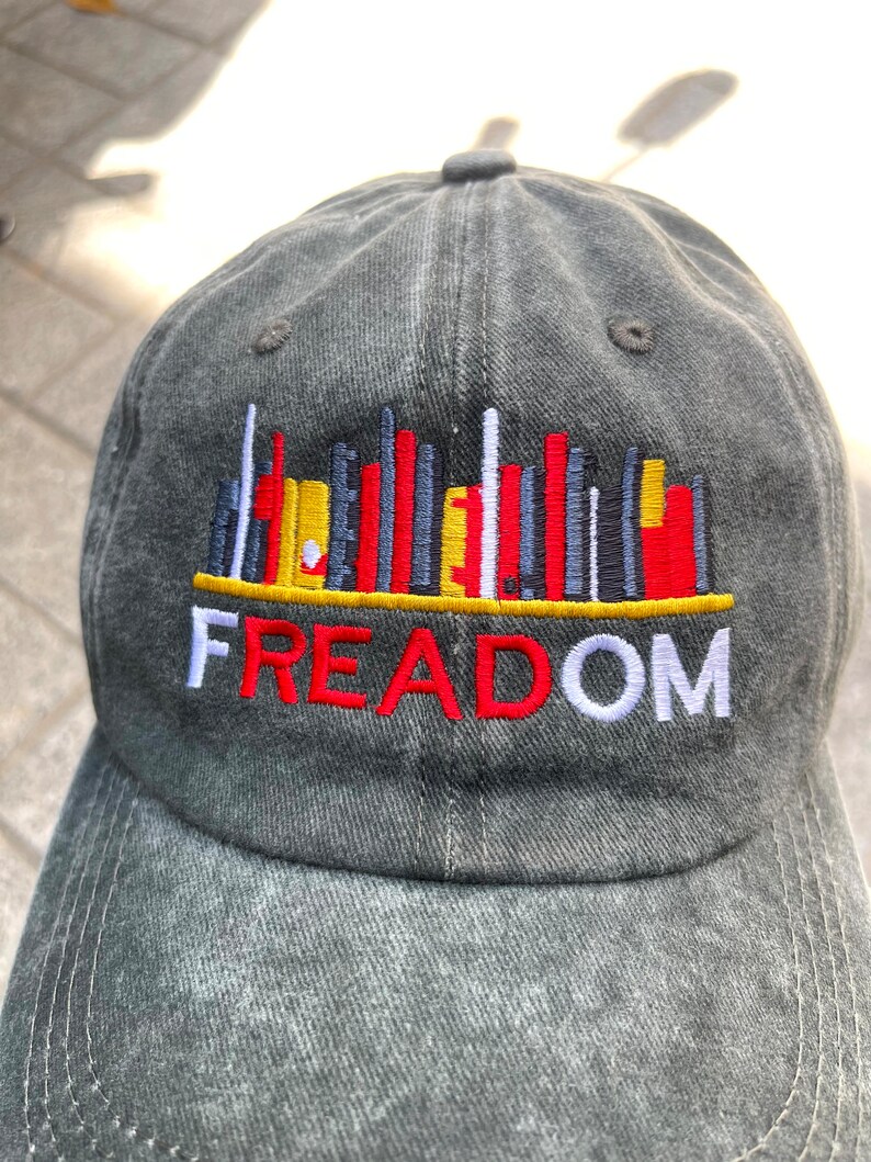 May include: A gray denim baseball cap with a colorful graphic of a city skyline and the word "FREEDOM" embroidered in red, white, and yellow.