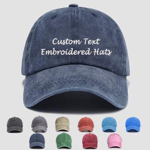 May include: A dark blue baseball cap with a distressed finish featuring the white embroidered text Custom Text Embroidered Hats on the front panel. Below the main cap, a grid displays ten additional baseball caps in various solid colors.