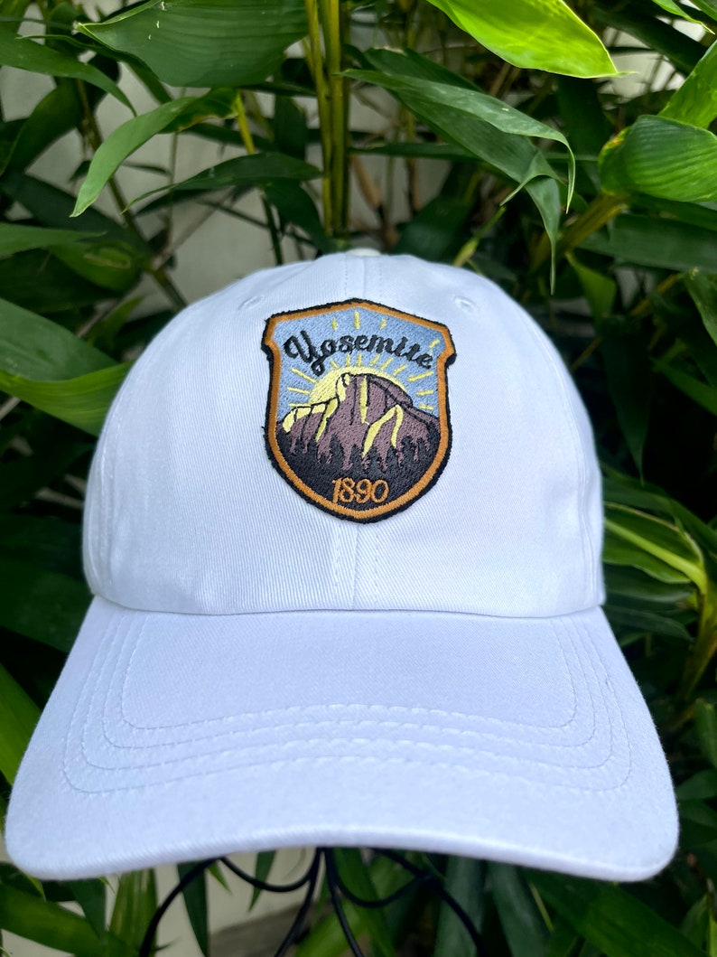 May include: White baseball cap with a brown and black embroidered patch featuring a mountain scene and the text "Yosemite 1890".