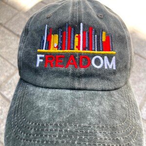 May include: A black denim baseball cap with a colorful cityscape graphic and the word "FREEDOM" embroidered in red, white, and yellow.