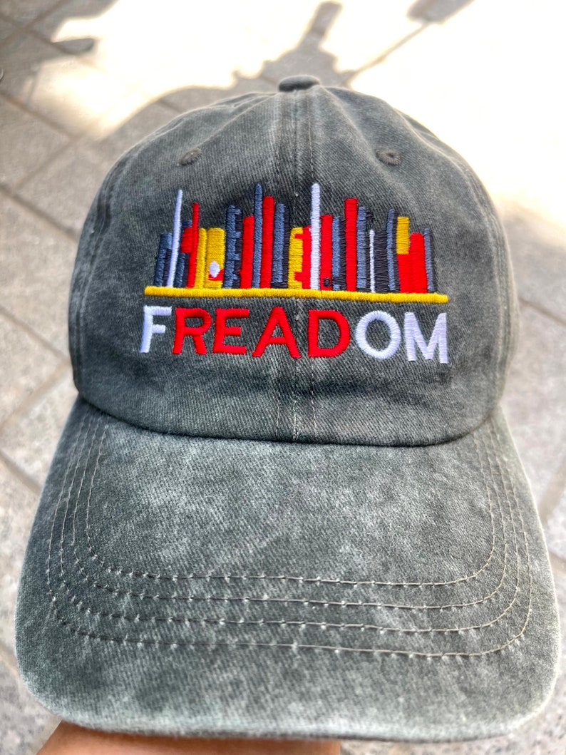May include: A black denim baseball cap with a colorful cityscape graphic and the word "FREEDOM" embroidered in red, white, and yellow.