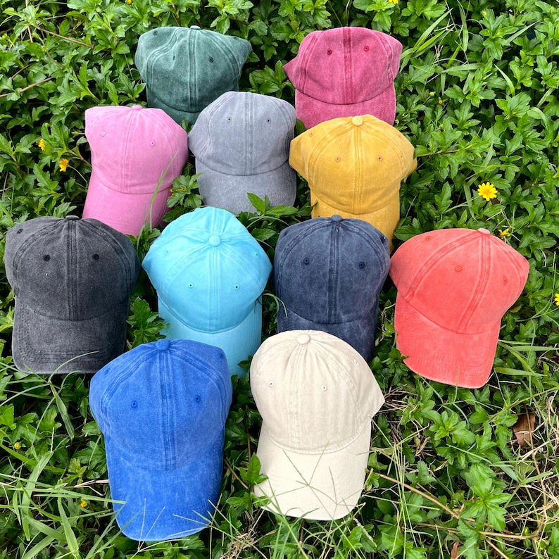 May include: A collection of eleven baseball caps in various colors including dark green, magenta, pink, gray, yellow, black, light blue, navy blue, bright blue, coral, and beige. Each cap features a six-panel design with a curved brim and button top.