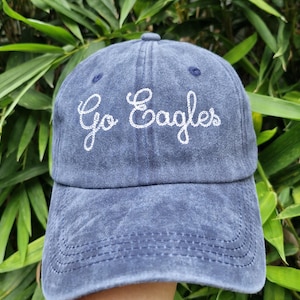 Könnte beinhalten: Eine blaue Baseballkappe aus Denim mit weiß gesticktem Text, der "Go Eagles" lautet.