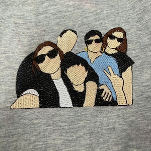 May include: A heather gray fabric featuring an embroidered graphic of four figures standing together. The figures wear black and blue shirts, with three wearing black sunglasses. One figure makes a peace sign with their hand, and another wears gold hoop earrings.