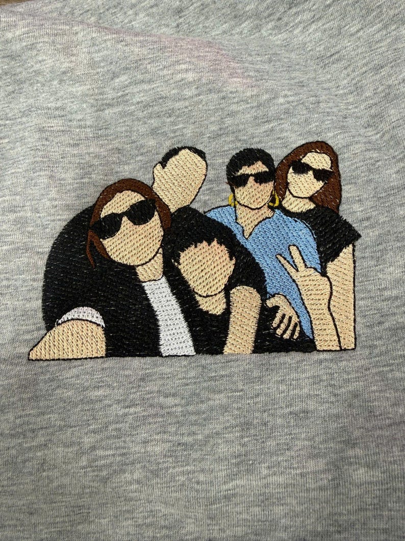 May include: A heather gray fabric featuring an embroidered graphic of four figures standing together. The figures wear black and blue shirts, with three wearing black sunglasses. One figure makes a peace sign with their hand, and another wears gold hoop earrings.