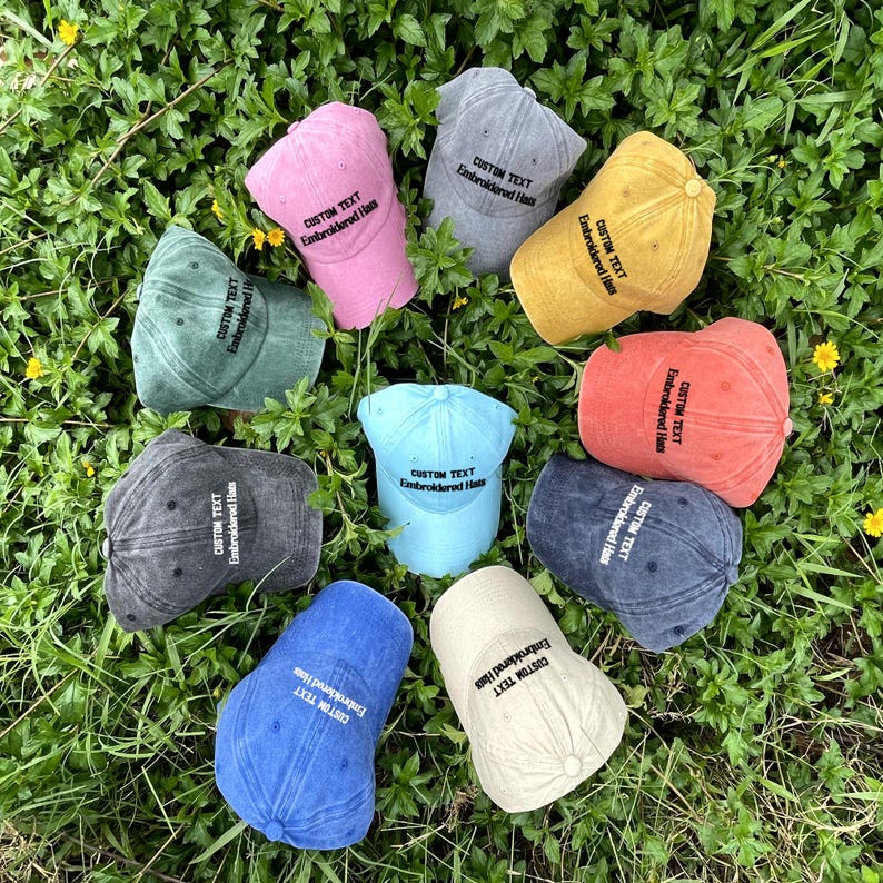 K&ouml;nnte beinhalten: Zehn Baseballkappen in verschiedenen Farben, jede mit dem Text "CUSTOM TEXT Embroidered Hats" auf der Vorderseite gestickt.