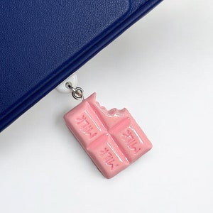 May include: A pink chocolate bar bookmark with a bite taken out of it. The bookmark has the word "Milka" printed on it.