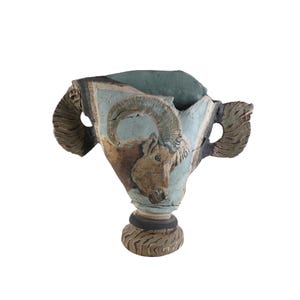 Può includere: Vaso in ceramica con disegno a testa di ariete. Il vaso ha uno sfondo azzurro chiaro con una testa di ariete marrone al centro. Le maniglie e la base sono strutturate con toni marroni e grigi.