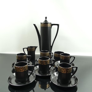 Può includere: Set da caffè nero e oro con teiera, lattiera e sei tazze e piattini. Le tazze e i piattini hanno un motivo geometrico.