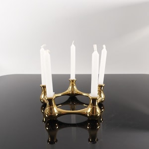 Könnte beinhalten: Eine weiße Keramiktasse mit schwarzem Henkel und dem Text "But First, Coffee" in fetter, schwarzer Schrift. Die Tasse steht vor einem verschwommenen Hintergrund, der eine gemütliche Umgebung suggeriert.