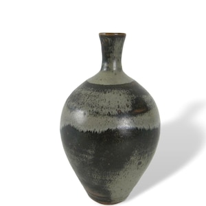 Könnte beinhalten: Eine graue und schwarze Keramikvase mit rundem Körper und schmalem Hals. Die Vase hat eine gesprenkelte Glasur und einen braunen Rand.