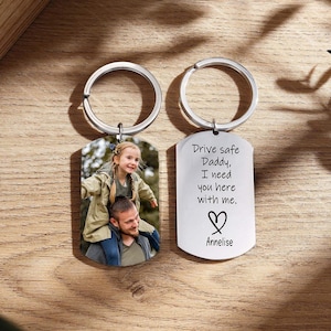 May include: Two silver keychains. One keychain features a photo of a man and a child. The other keychain has the text "Drive safe Daddy, I need you here with me." with a heart and the name "Annelise."