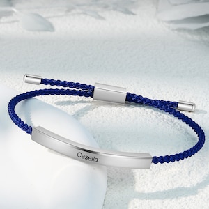Könnte beinhalten: Ein verstellbares blaues Armband aus Kordel mit einer silbernen Leiste, auf der der Name "Casella" eingraviert ist.