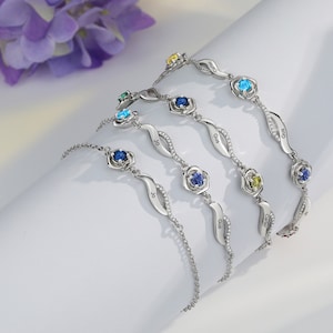 May include: Five silver bracelets with delicate chains and rose-shaped charms. Each charm features a different colored gemstone and a personalized nameplate: Gus, Carter, Jo, Gus, and Gus.