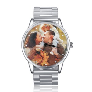 May include: A silver wristwatch with a round face featuring a photo of a family of three. The photo shows a man and woman with a child on the man's shoulders. The watch has a silver metal band.