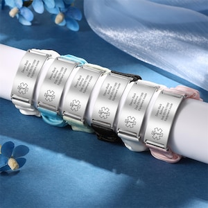 May include: Six silver medical alert bracelets with different colored bands. Each bracelet has a star of life symbol and the text "Devon Black, Asthma, Dob 09/09/1999, Equipment inside". The bands are white, light blue, light green, black, white, and pink.