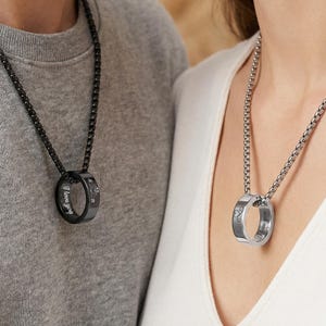 May include: Two matching ring necklaces. One is black with the words "I love you" and a heart symbol. The other is silver with the same text and a heart symbol. Both necklaces are on chain necklaces.