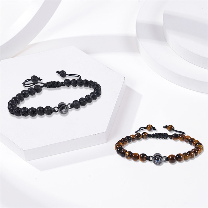 Pu&ograve; includere: Due braccialetti con perline e chiusure regolabili in corda. Un braccialetto &egrave; realizzato con perline di roccia lavica nera e l'altro con perline di occhio di tigre marrone. Entrambi i braccialetti presentano un ciondolo d'argento con un design di occhio malocchio nero.