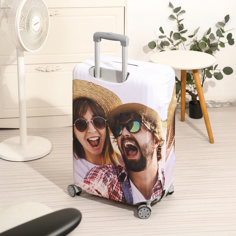 May include: White suitcase cover with a photo of two people wearing sunglasses and hats. The photo shows the couple smiling and looking at the camera.