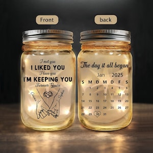 Puede incluir: Dos tarros de cristal con tapas plateadas, uno con el texto "I met you, I liked you, I love you, I'm keeping you forever yours" y un dibujo de manos. El otro tarro tiene un calendario de enero de 2025.