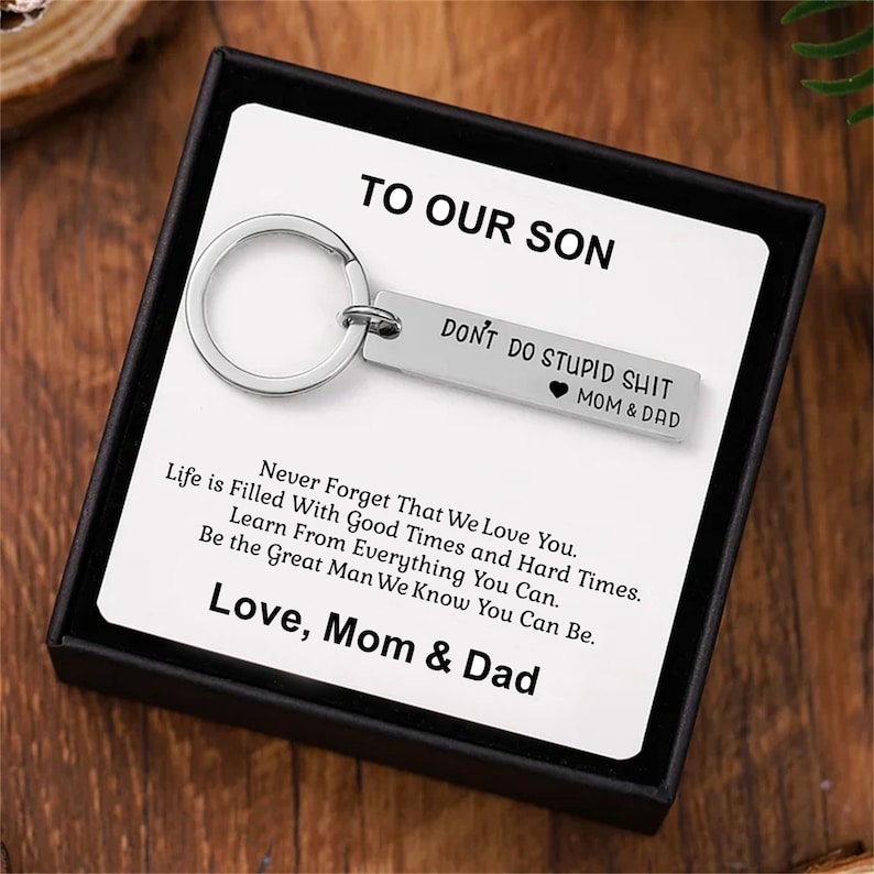 May include: A black gift box with a silver keychain inside. The keychain has a silver tag that reads 'Don't do stupid shit Mom & Dad.' The box also contains a card that reads 'To our son, Never forget that we love you. Life is filled with good times and hard times. Learn from everything you can. Be the great man we know you can be. Love, Mom & Dad.'