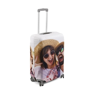 May include: A white suitcase cover with a photo of three people smiling and wearing sunglasses. The people are wearing casual clothing and hats. The suitcase cover has a zipper closure and a handle.
