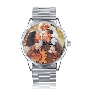 K&ouml;nnte beinhalten: Eine silberne Armbanduhr mit einem runden Zifferblatt, auf dem ein Foto einer dreik&ouml;pfigen Familie zu sehen ist. Das Foto zeigt einen Mann und eine Frau mit einem Kind auf den Schultern des Mannes. Die Uhr hat ein silbernes Metallband.