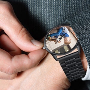 K&ouml;nnte beinhalten: Eine schwarze Armbanduhr mit einem Edelstahlband. Das Zifferblatt der Uhr zeigt ein Foto eines Kindes, das einen Hund h&auml;lt.