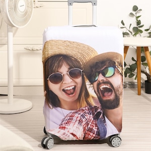 May include: A white suitcase cover with a photo of a couple wearing sunglasses and smiling. The couple is wearing casual clothing and is taking a selfie. The suitcase cover is designed to protect and personalize luggage.