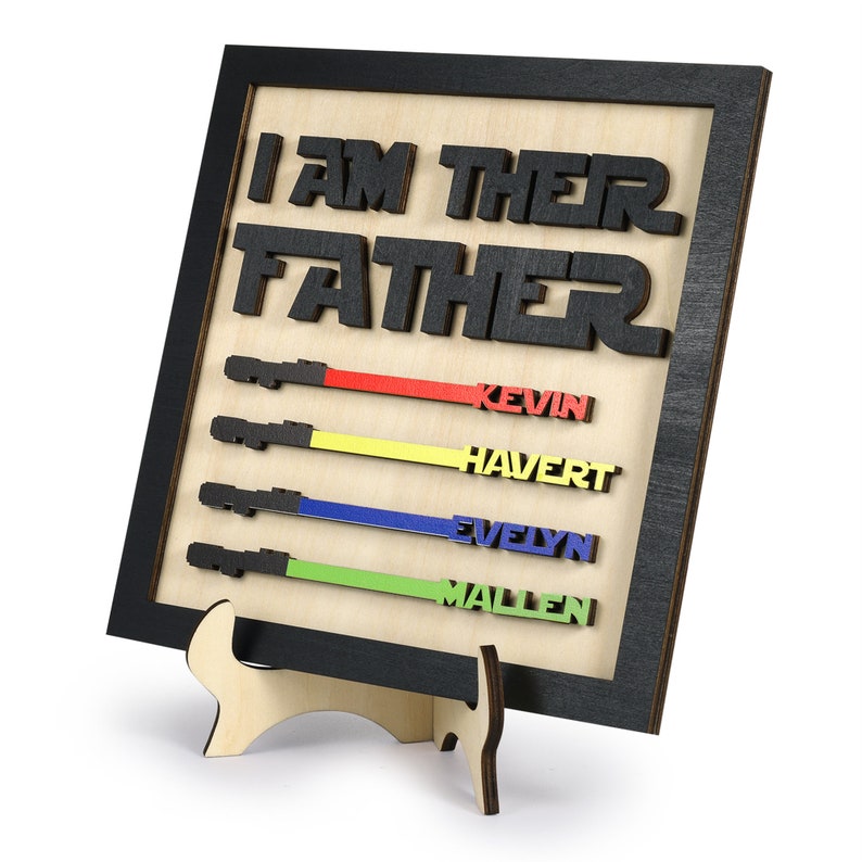 Puede incluir: Un letrero de madera con el texto "Soy su padre" en letras negras. El letrero tiene cuatro sables de luz con los nombres Kevin, Havert, Evelyn y Mallen escritos en ellos en diferentes colores.