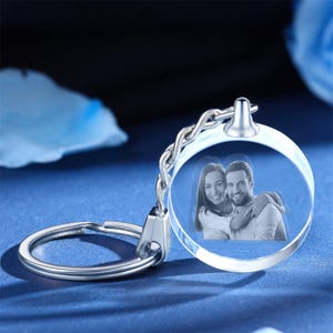 May include: A silver keychain with a clear crystal charm. The charm has a 3D engraved image of a couple embracing.